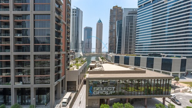 A modern building with a glass facade and a sign reading 'SELECT GROUP'. - Refined Studio with Sweeping Dubai Water Canal and City Views (Dubai)