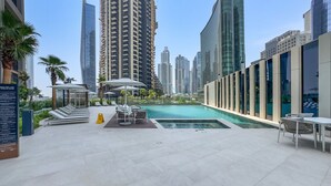 A rooftop pool area with lounge chairs and umbrellas, surrounded by high-rise buildings. - Refined Studio with Sweeping Dubai Water Canal and City Views (Dubai)