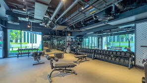 A gym with exercise equipment, weight racks, and large windows. - Refined Studio with Sweeping Dubai Water Canal and City Views (Dubai)