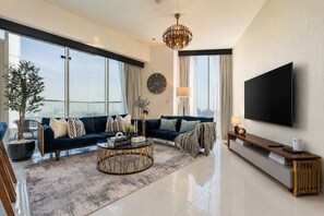 A modern living room with a large sofa set, a coffee table, and a flat-screen TV mounted on the wall. - High-Floor 2BR with Skyline Views, Moments from Dubai Butterfly Garden (Dubai)