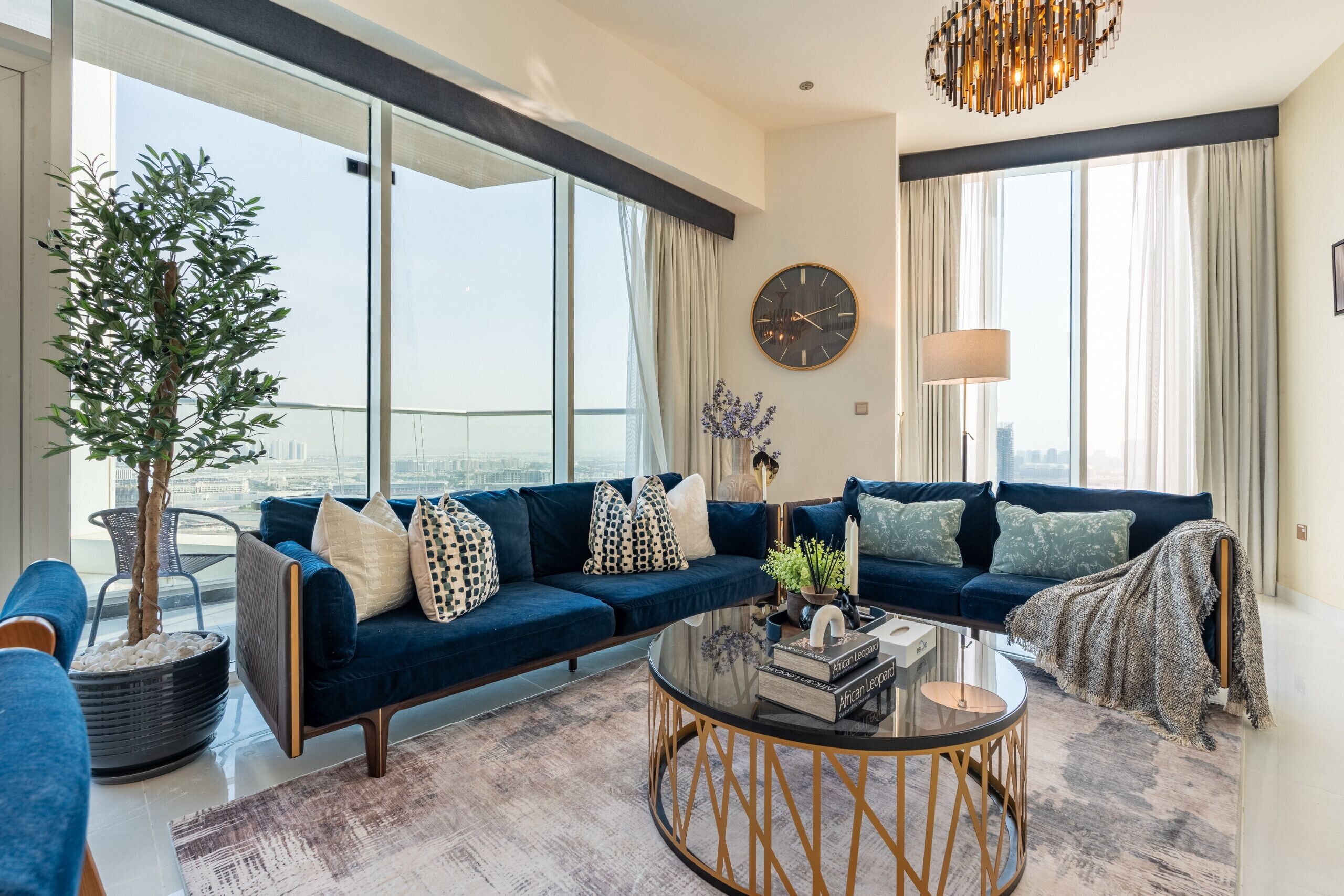 Een moderne woonkamer met een blauwe bank, een ronde salontafel en een groot raam met uitzicht op de stad.
