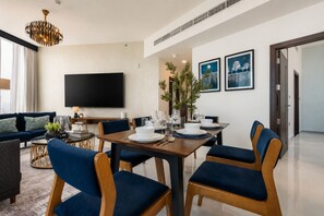 Een moderne woonkamer met een flatscreen-tv, een eettafel gedekt voor vier personen en een groot raam met gordijnen.