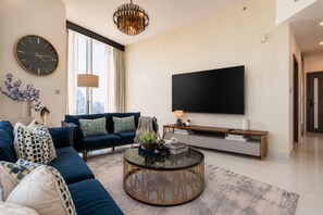A modern living room with a blue sofa, a round coffee table, a flat-screen TV, and a chandelier. - High-Floor 2BR with Skyline Views, Moments from Dubai Butterfly Garden (Dubai)