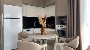 A modern kitchen with white cabinetry, a white refrigerator, and a dining area with a round table and chairs. - Qoople Green Ocean A49 - Cozy 1-bedroom apartment in Alanya (Alanya)