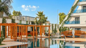 A pool area with wooden pergolas, lounge chairs, and a clear blue sky. - Qoople Green Ocean A49 - Cozy 1-bedroom apartment in Alanya (Alanya)