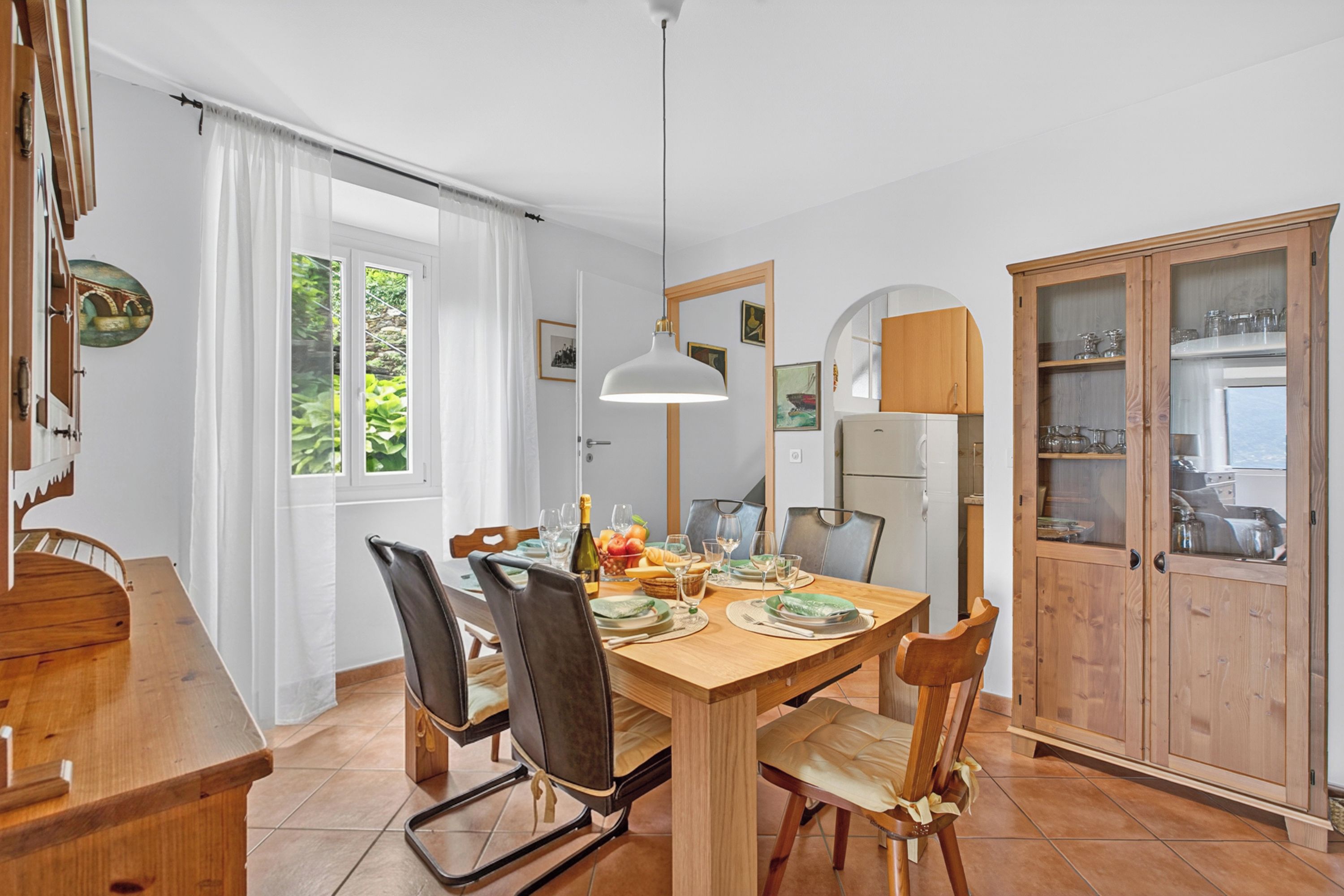 A dining area with a wooden table, chairs, and a hanging light fixture.