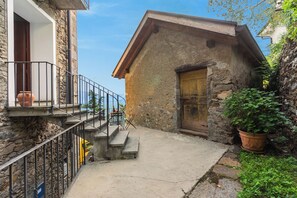A stone building with a wooden door, a balcony with a railing, and a potted plant. - Casa Berta Brissago 2 With Balcony for Six (Brissago)