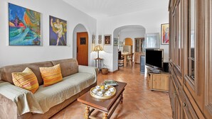 Ein Wohnzimmer mit Sofa, Couchtisch, Fernseher und Kunstwerken an den Wänden.