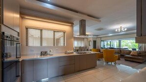 A modern kitchen with a central island, built-in appliances, and a dining area with yellow chairs. - The House Guest House (Sabi River Eco Estate)