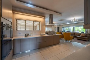 A modern kitchen with a central island, built-in appliances, and a dining area with yellow chairs. - The House Guest House (Sabi River Eco Estate)