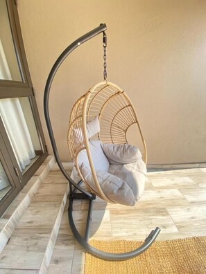 A room with a hanging chair with cushions, a window with curtains, and a wooden floor. - The House Guest House (Sabi River Eco Estate)
