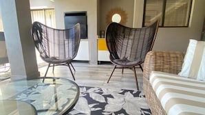 A room with a glass table, two wicker chairs, a striped sofa, and a patterned carpet. - The House Guest House (Sabi River Eco Estate)