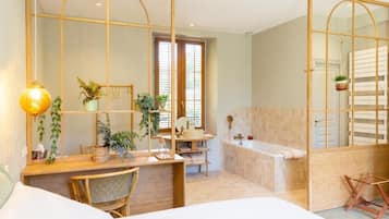 A modern bathroom with a bathtub, a sink, and a mirror. There are plants and a lamp on the vanity.