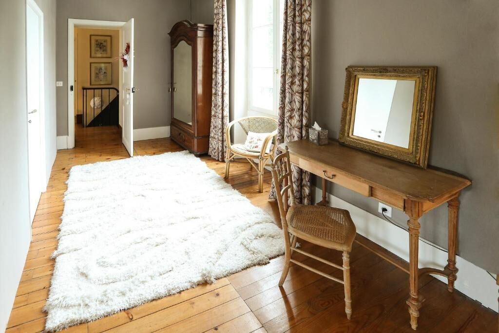 Een kamer met een houten bureau, een stoel, een spiegel, een wit pluizig vloerkleed, een kledingkast en een trap naar een andere kamer.