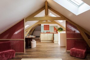 Una habitación estilo loft con techo inclinado, vigas de madera, zona de cocina y una mesa de comedor con sillas.