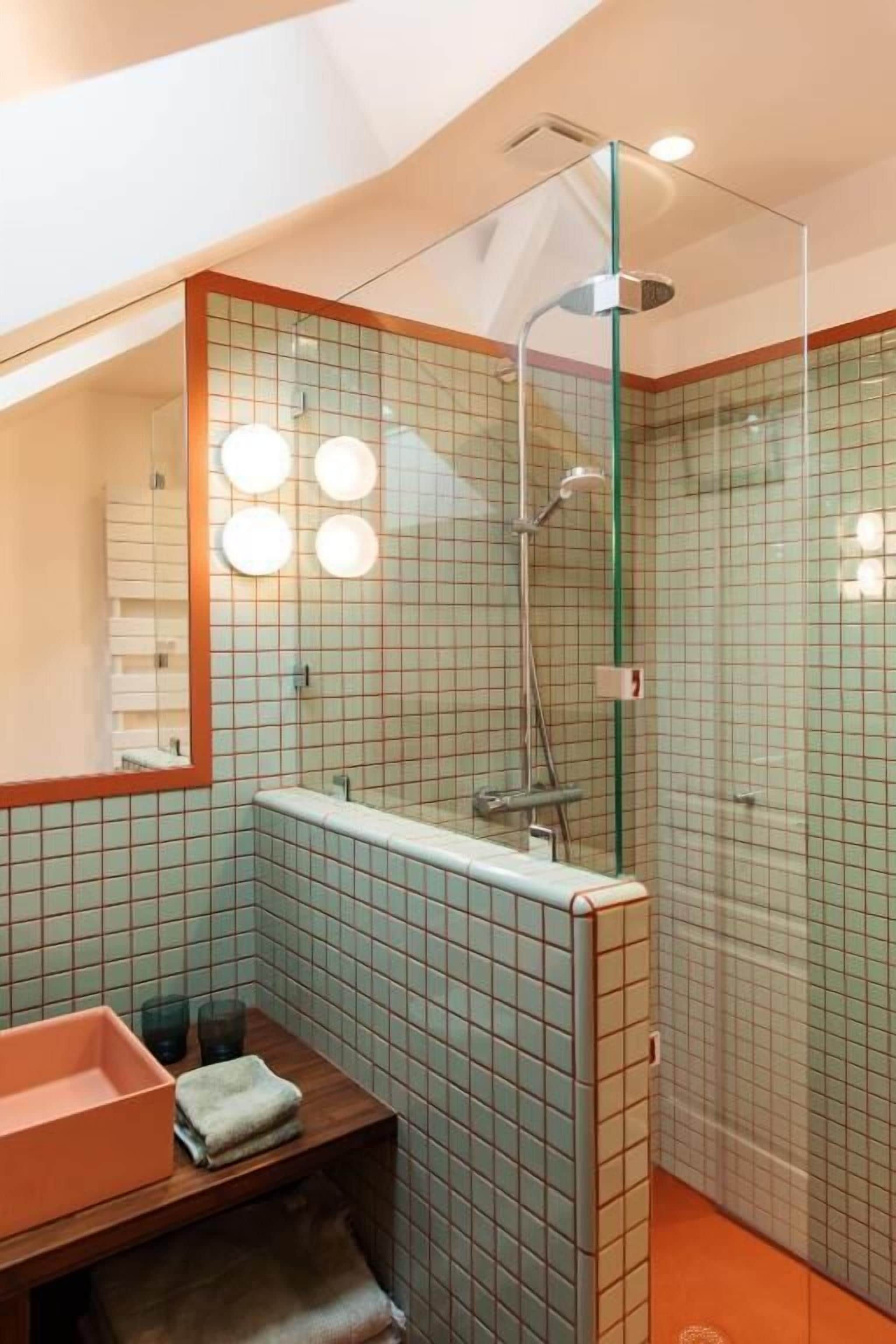 Un baño moderno con cabina de ducha de vidrio, un banco de madera y un espejo con iluminación.