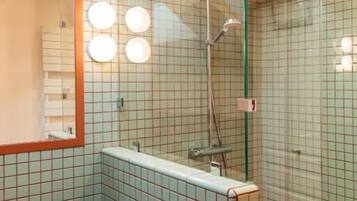 Un baño moderno con cabina de ducha de vidrio, un banco de madera y un espejo con iluminación.