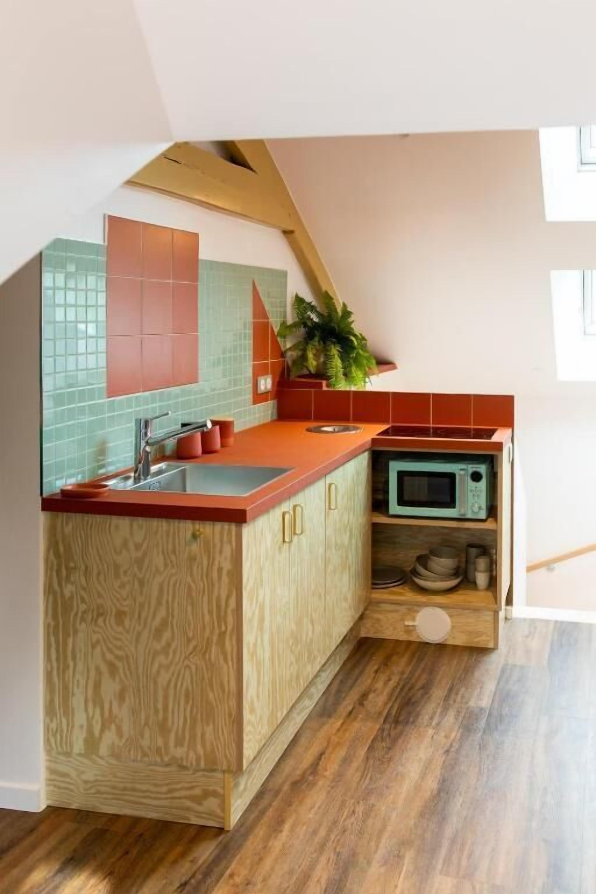 Een kleine keuken met een houten kastje, een rode aanrecht en een magnetron.