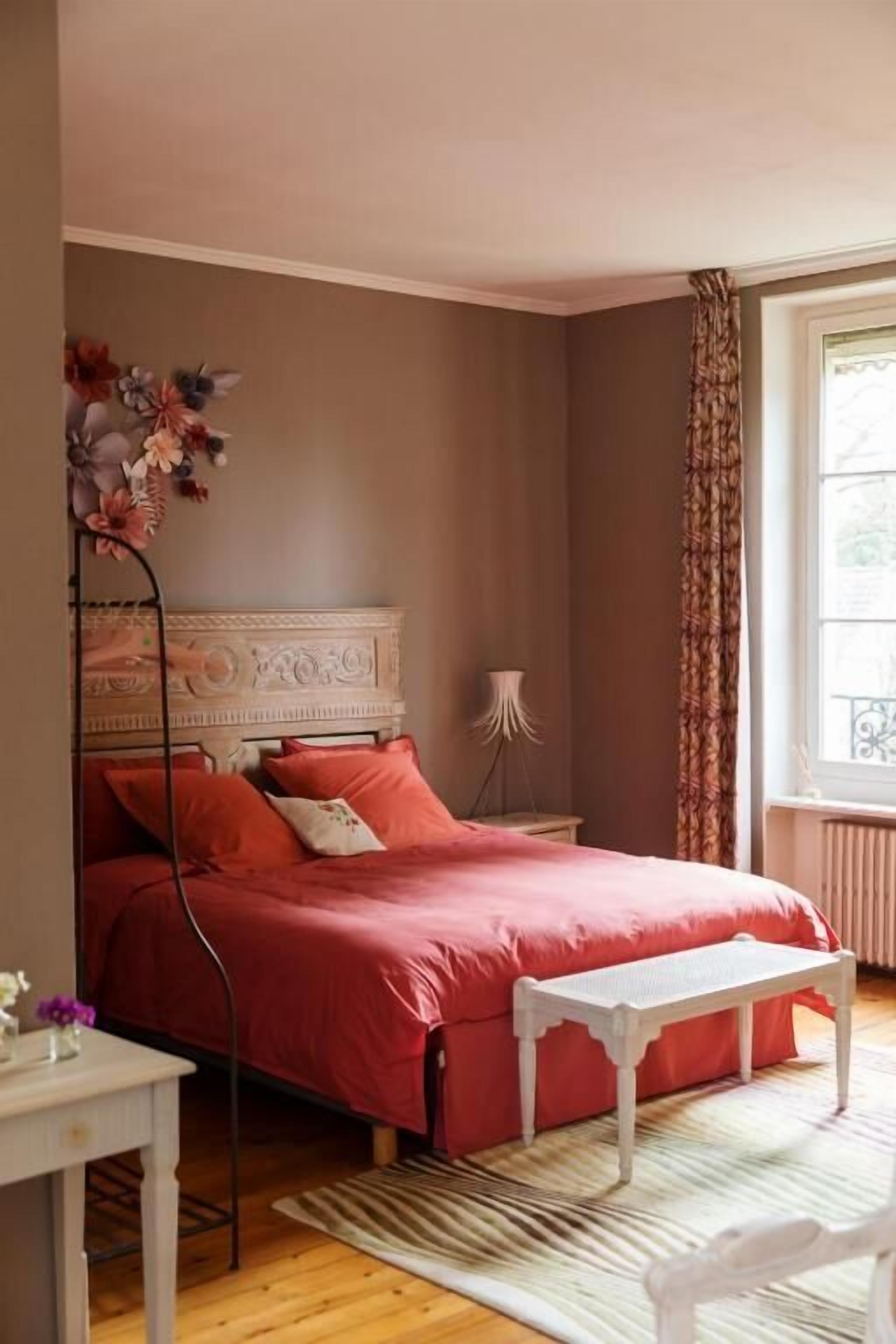 Une chambre à coucher avec un lit, une table de chevet, une lampe et une fenêtre avec des rideaux.