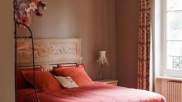 Une chambre à coucher avec un lit, une table de chevet, une lampe et une fenêtre avec des rideaux.