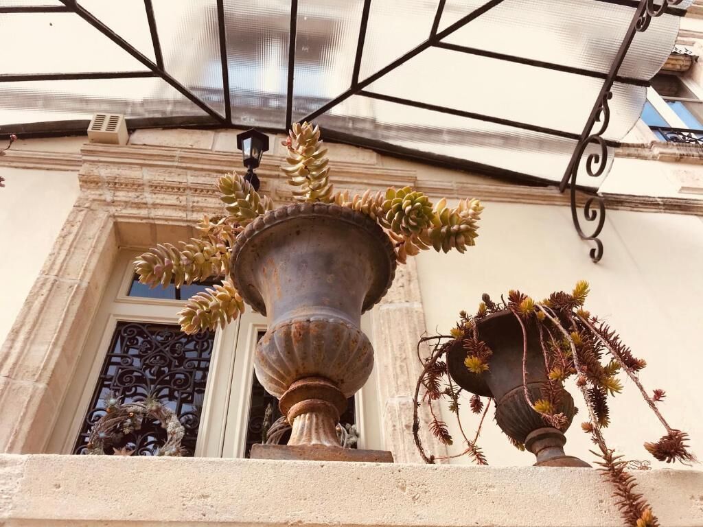 Una jardinera grande al aire libre con suculentas y una maceta más pequeña con plantas colgantes, ambos en un balcón con barandilla de hierro forjado.