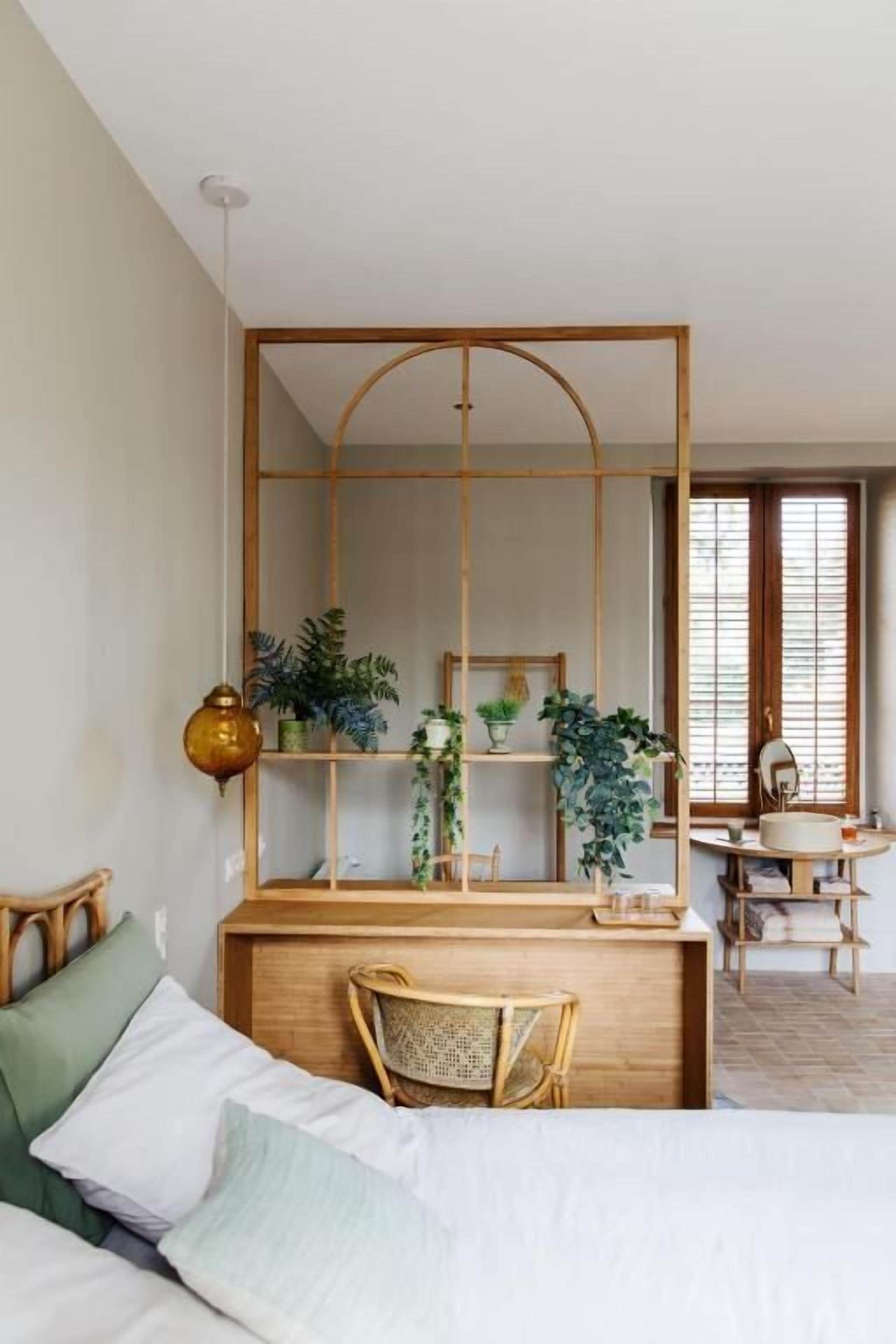 Un dormitorio con cama, escritorio y silla. Hay plantas en el escritorio y una ventana con persianas.