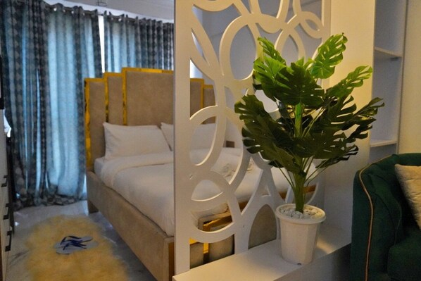A bedroom with a bed, a decorative white partition, and a potted plant. - Smart Homes- City Haven (Nairobi)