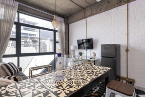 Ein modernes Wohnzimmer mit großem Fenster, einem Flachbildfernseher, einem Kühlschrank und einem Tisch mit Muster.