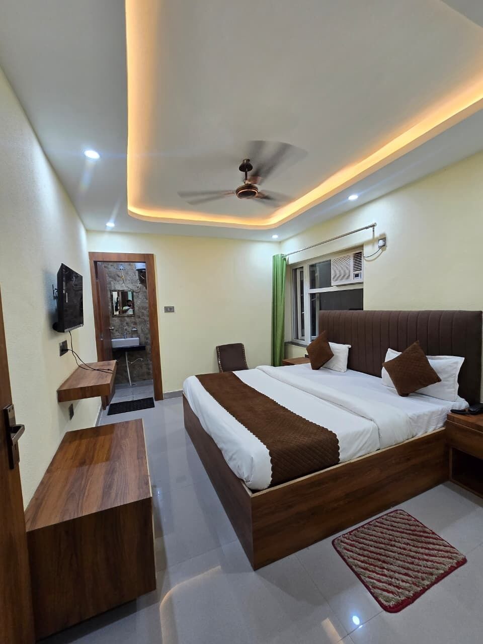 A modern hotel room with a large bed, a desk, a mirror, and a ceiling fan.
