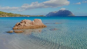 Mar azul cristalina con un promontorio rocoso en primer plano y una montaña al fondo.