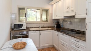 Una cocina con armarios blancos, microondas, lavabo y una ventana con persianas.