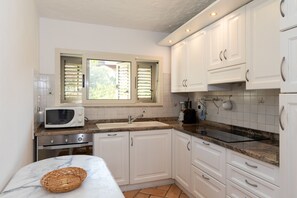 Eine Küche mit weißen Schränken, einer Mikrowelle, einem Spülbecken und einem Fenster mit Jalousien.
