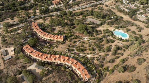 Vista aérea de un área residencial con un edificio curvo, piscina y follaje circundante.