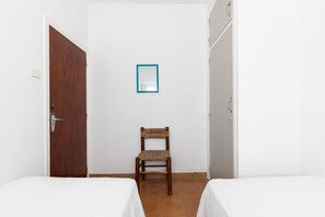 A small, simple room with two beds, a wooden chair, a door, and a wall-mounted mirror. - Apartment next to Salou's Ponent Beach (Salou)