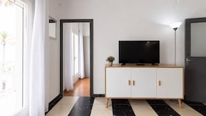 Un salon moderne avec un téléviseur à écran plat posé sur un meuble en bois, une plante en pot et une porte donnant sur une autre pièce.