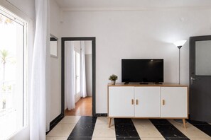 Ein modernes Wohnzimmer mit einem Flachbildfernseher auf einem Holzschrank, einer Topfpflanze und einer Tür zu einem anderen Raum.