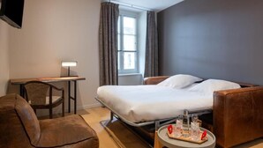 Habitación de hotel con cama, escritorio, silla, televisor y ventana con cortinas.