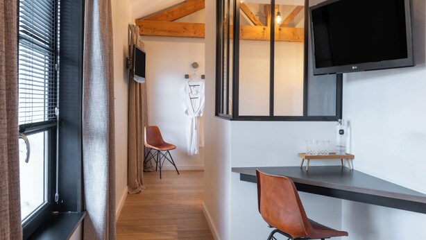 Una habitación moderna con televisión de pantalla plana en la pared, una silla de madera, una mesita con una botella y una bata colgada en un perchero.