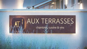 Señal que dice 'AUX TERRASSES' con el texto 'chambres, cuisine & vins', indicando habitaciones de hotel, comidas y vinos.