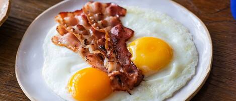 A breakfast plate with eggs and bacon, a glass of orange juice, and pancakes on a wooden table.
