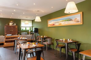 A dining area with tables, chairs, and a painting on the wall. - Hotel Aux Terrasses  (Tournus)
