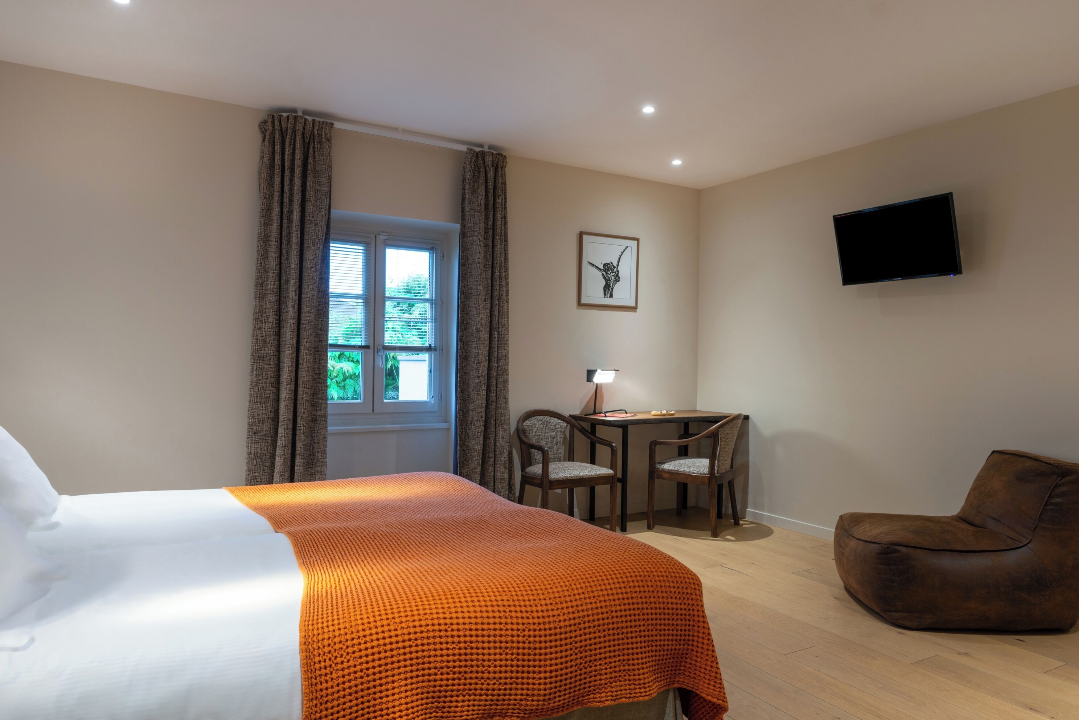 A hotel room with a bed, a desk, two chairs, a television, and a window with curtains.