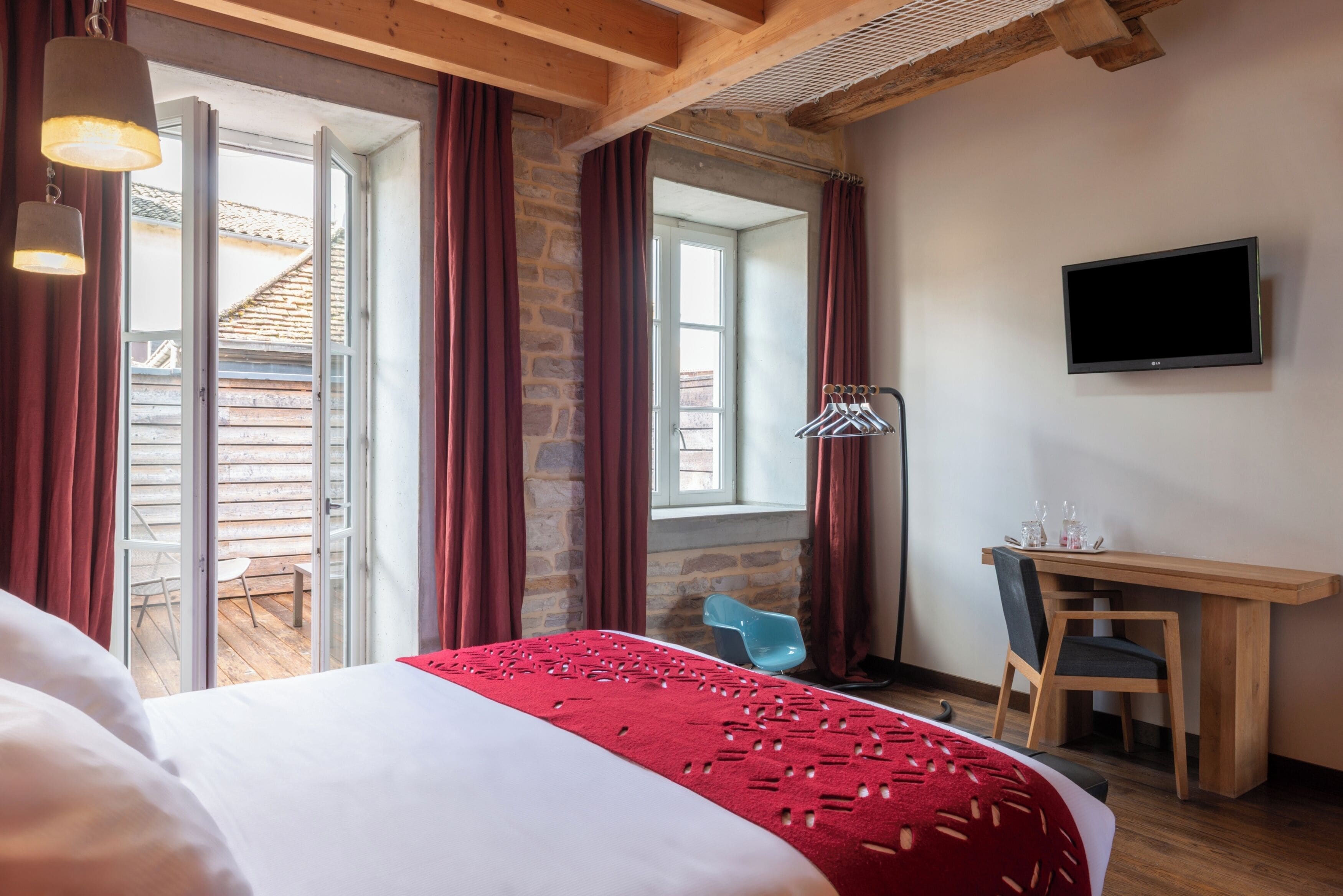 Habitación de hotel con cama, escritorio, silla, televisión y balcón con vista a un edificio.