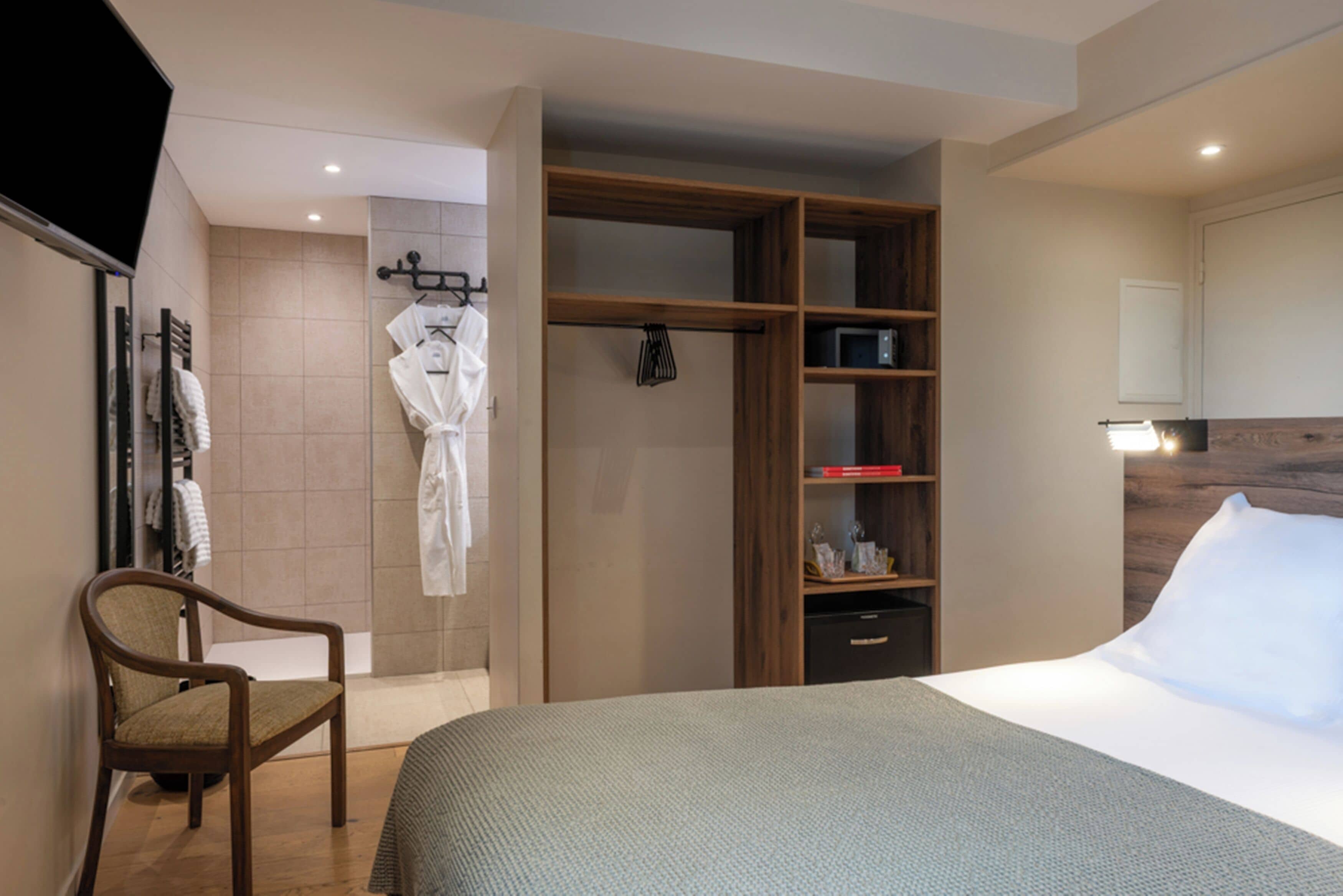 Habitación de hotel con cama, armario de madera, una silla y baño con toallero.
