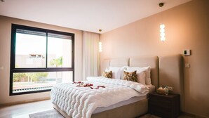 Ein modernes Schlafzimmer mit einem großen Bett, einem Nachttisch, einem Fenster mit Jalousien und einer Wandleuchte.