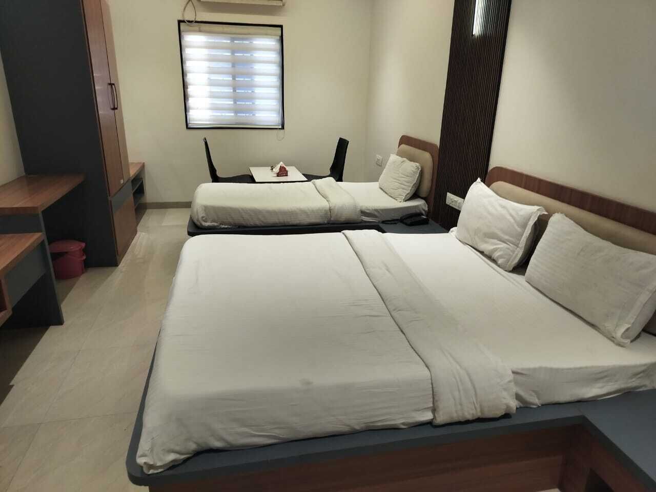 Habitación de hotel con dos camas, un escritorio, una silla y una ventana con persianas.