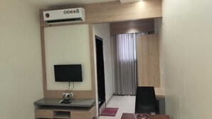 Habitación de hotel con televisor de pantalla plana en una pared de madera, un escritorio con silla, una mesita y una ventana con cortinas.