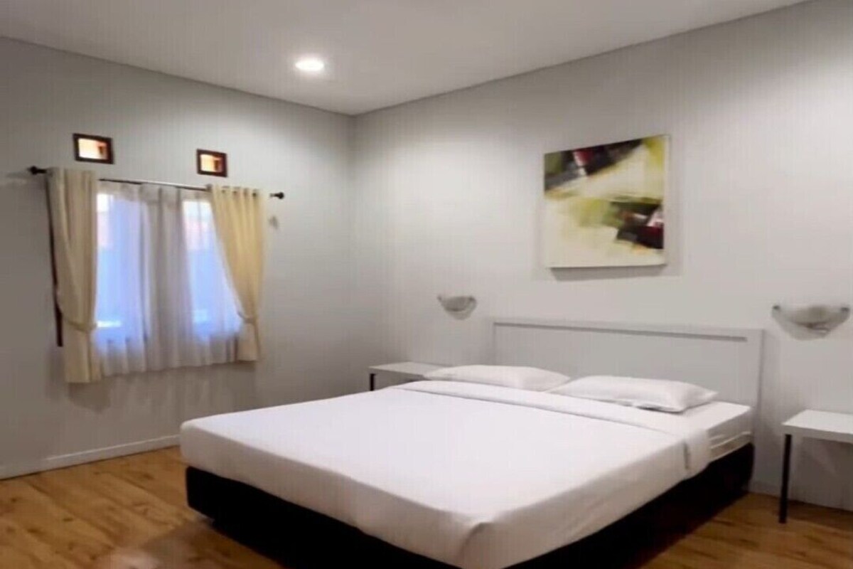 Ein Schlafzimmer mit einem großen Bett, einem Nachttisch, einer Wandleuchte und einem Fenster mit Vorhängen.