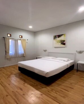 Ein Schlafzimmer mit einem großen Bett, einem Nachttisch, einer Wandleuchte und einem Fenster mit Vorhängen.