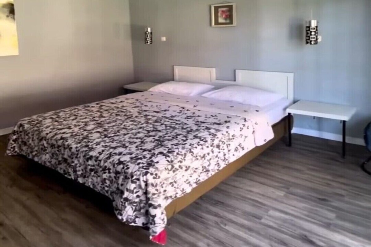 Ein Schlafzimmer mit einem Bett, einem Nachttisch, einer Wandleuchte und einem Bild.